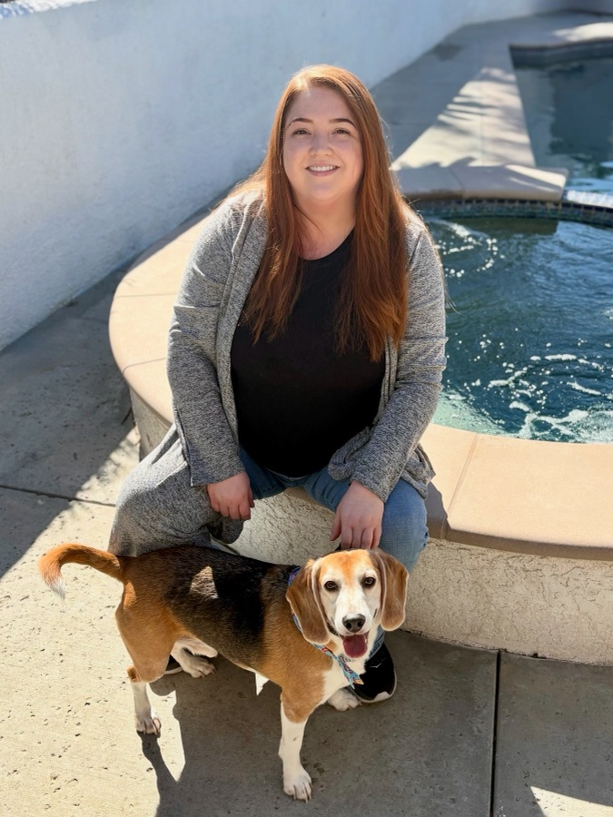 Sarah, owner and groomer at Coat & Tail Grooming, sitting by a pool with her beagle